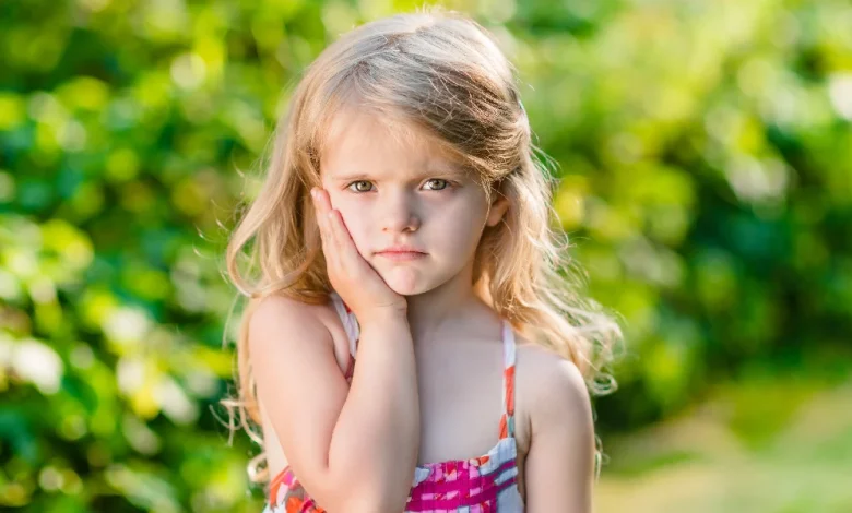 دخترکی که دستش را روی گونه اش گذاشته | آفت دهان کودک